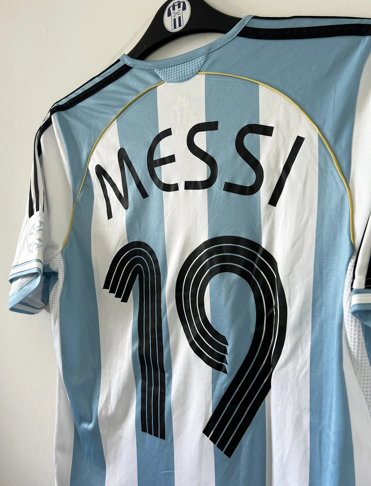 Maillot de foot vintage de l'argentine de la coupe du monde 2006. Le maillot est de couleur bleu et blanc. On peut retrouver l'équipementier adidas. Le maillot est floqué du numéro 19 Lionel Messi. Il s'agit d'un maillot authentique comportant les numéros 739802.