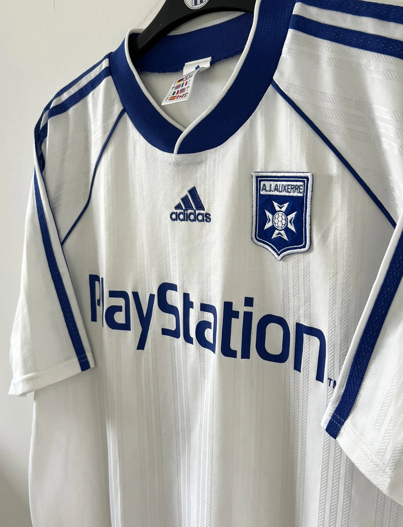 Maillot de foot vintage domicile blanc et bleu de l'AJ Auxerre de la saison 1999/2000. On peut retrouver l'équipementier adidas et le sponsor Playstation. Il s'agit d'un maillot authentique d'époque.