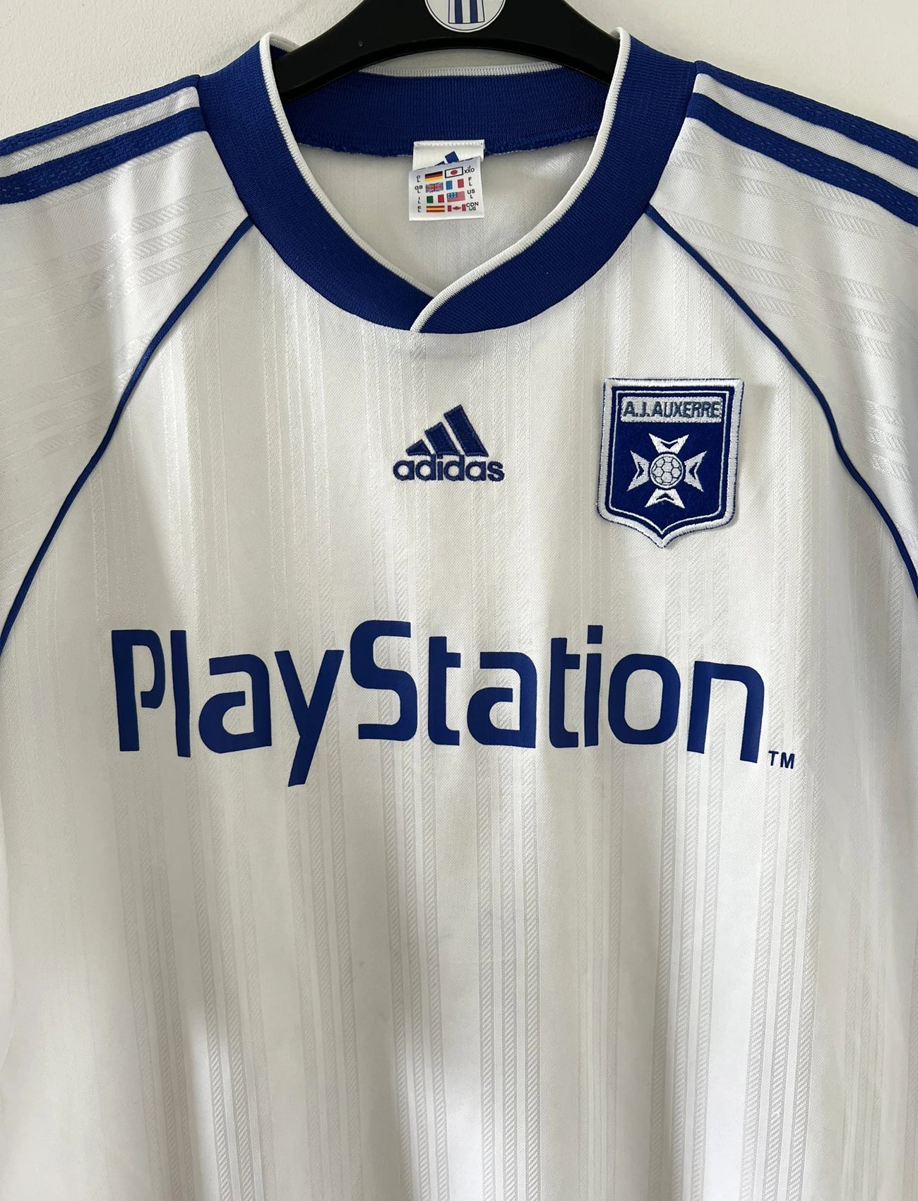 Maillot de foot vintage domicile blanc et bleu de l'AJ Auxerre de la saison 1999/2000. On peut retrouver l'équipementier adidas et le sponsor Playstation. Il s'agit d'un maillot authentique d'époque.