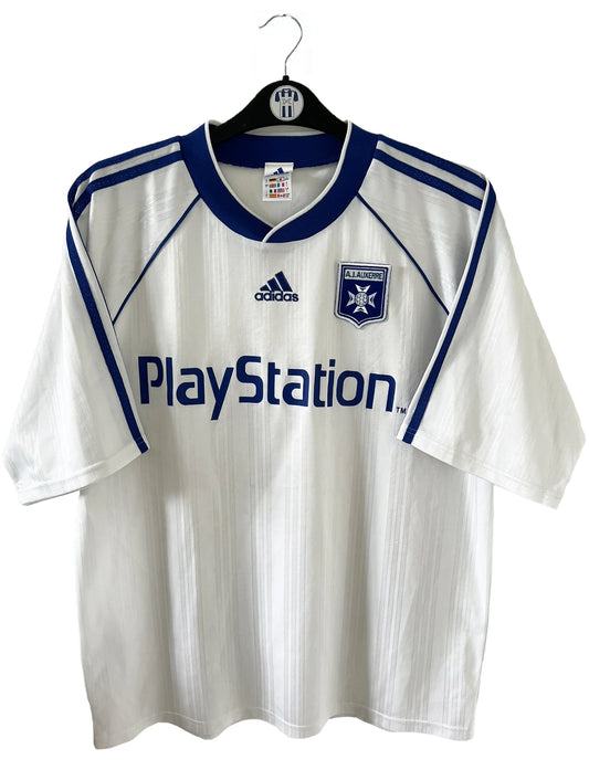 Maillot de foot vintage domicile blanc et bleu de l'AJ Auxerre de la saison 1999/2000. On peut retrouver l'équipementier adidas et le sponsor Playstation. Il s'agit d'un maillot authentique d'époque.