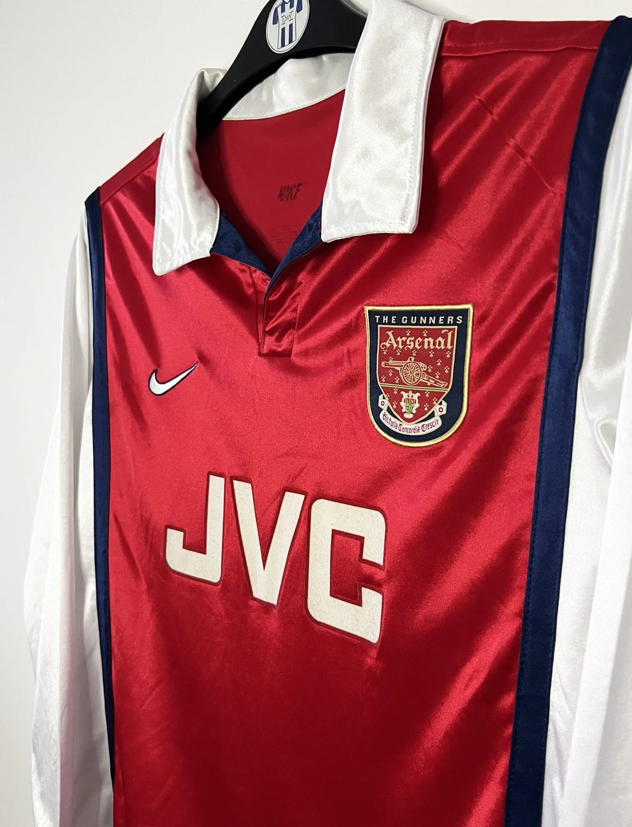 Maillot de foot vintage domicile rouge et blanc version manche longue d'Arsenal de la saison 1998/1999. On peut retrouver l'équipementier Nike et le sponsor JVC. Il s'agit d'un maillot authentique d'époque.