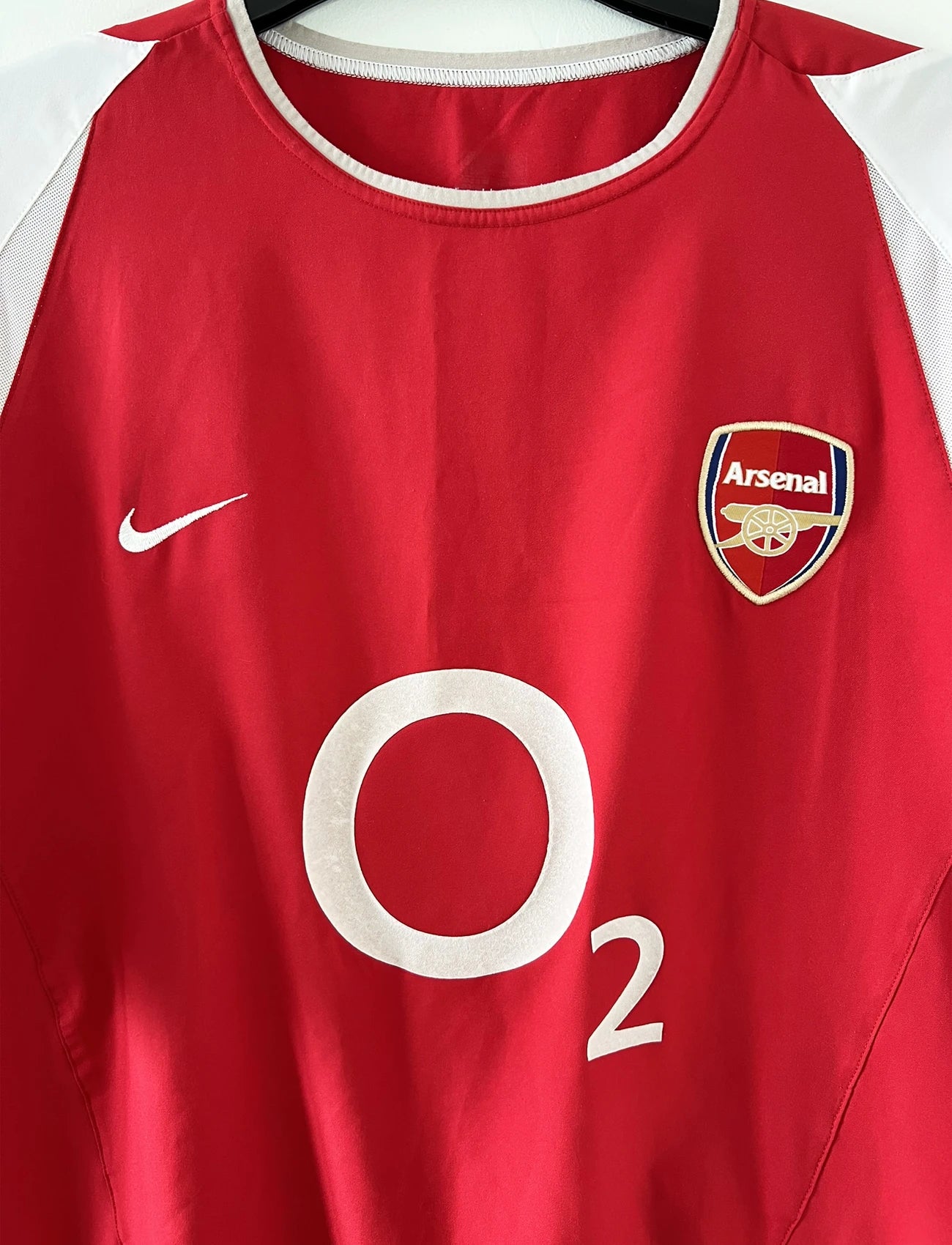 Maillot domicile Arsenal rouge et blanc de la saison 2002-2004. On peut retrouver l'équipementier nike et le sponsor O2. Il s'agit d'un maillot authentique d'époque comportant l'étiquette 184985