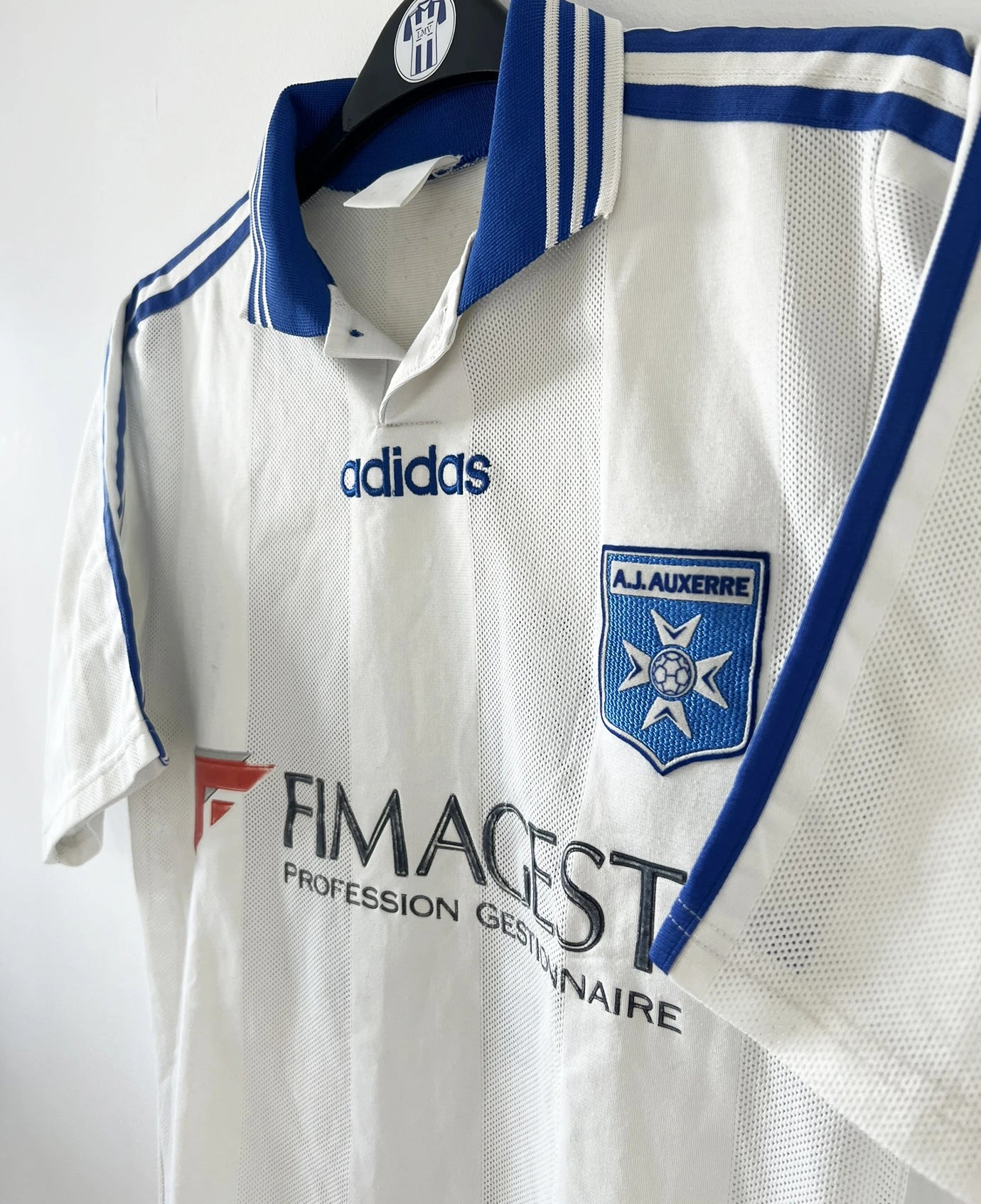 Maillot de foot vintage domicile blanc et bleu de l'AJ Auxerre de la saison 1997/1998. On peut retrouver l'équipementier adidas et le sponsor fimagest. Il s'agit d'un maillot authentique d'époque.