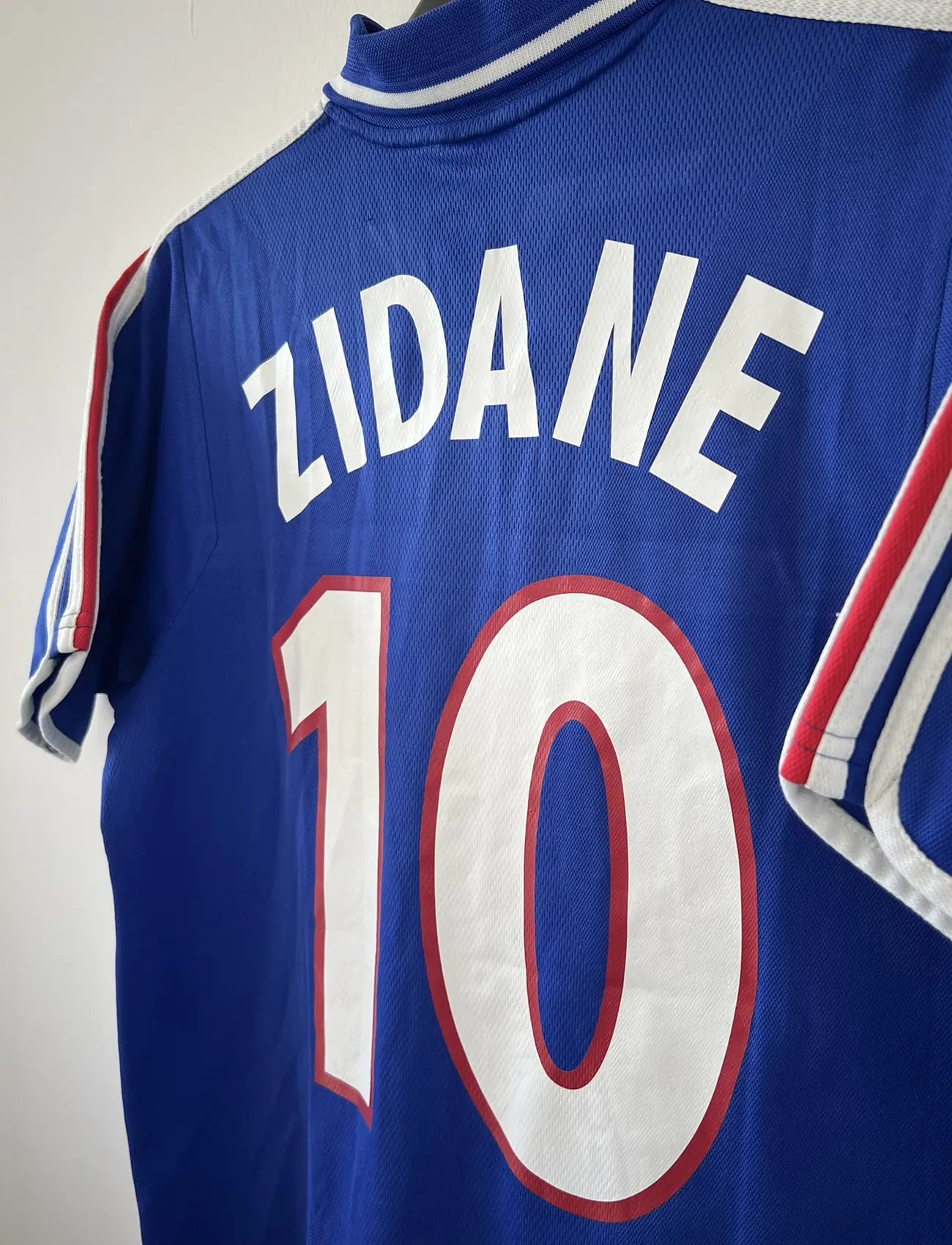 Maillot de foot vintage domicile de l'équipe de france 2000. Le maillot est de couleur bleu blanc et rouge. On peut retrouver l'équipementier adidas. Le maillot est floqué du numéro 10 Zinedine Zidane à l'avant et au dos du maillot. Il s'agit d'un maillot authentique comportant les numéros 647194.