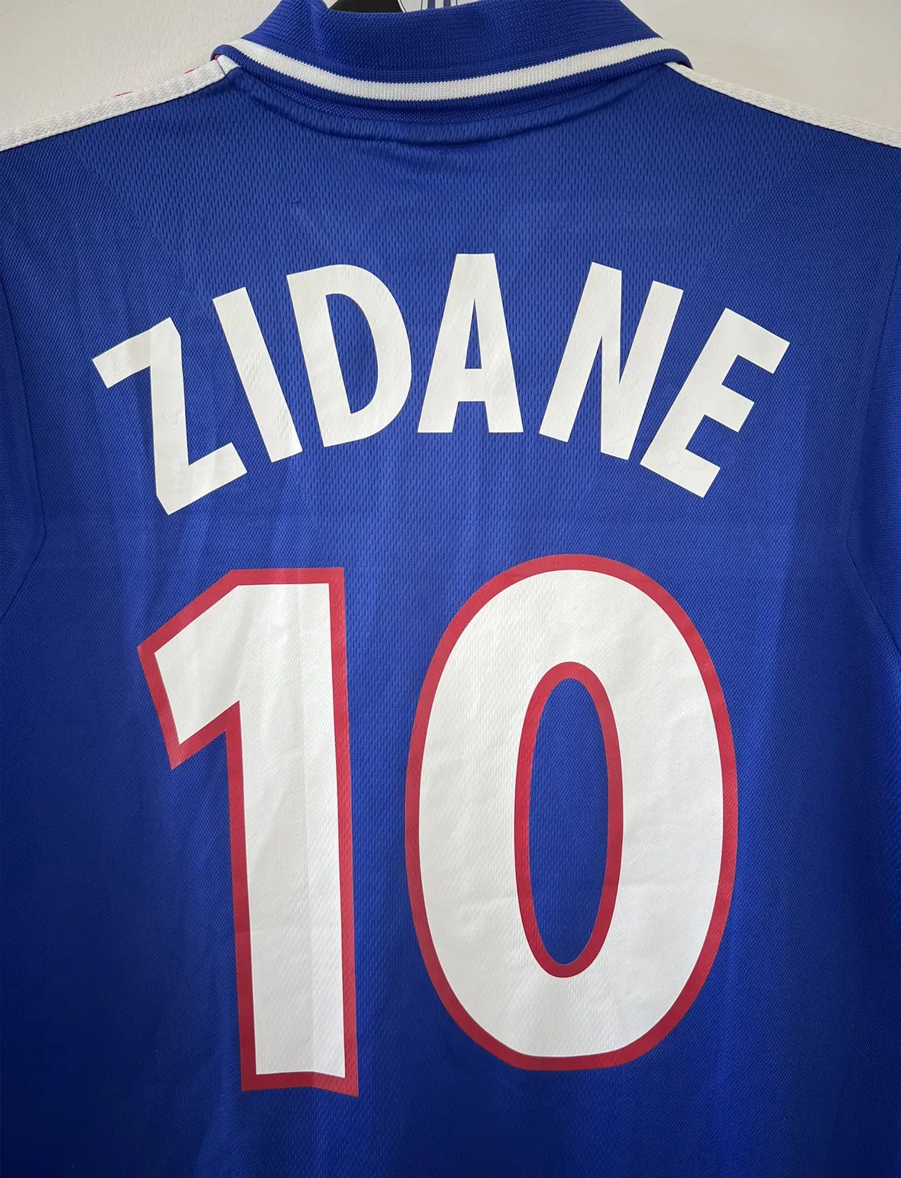 Maillot de foot vintage domicile de l'équipe de france 2000. Le maillot est de couleur bleu blanc et rouge. On peut retrouver l'équipementier adidas. Le maillot est floqué du numéro 10 Zinedine Zidane à l'avant et au dos du maillot. Il s'agit d'un maillot authentique comportant les numéros 647194.