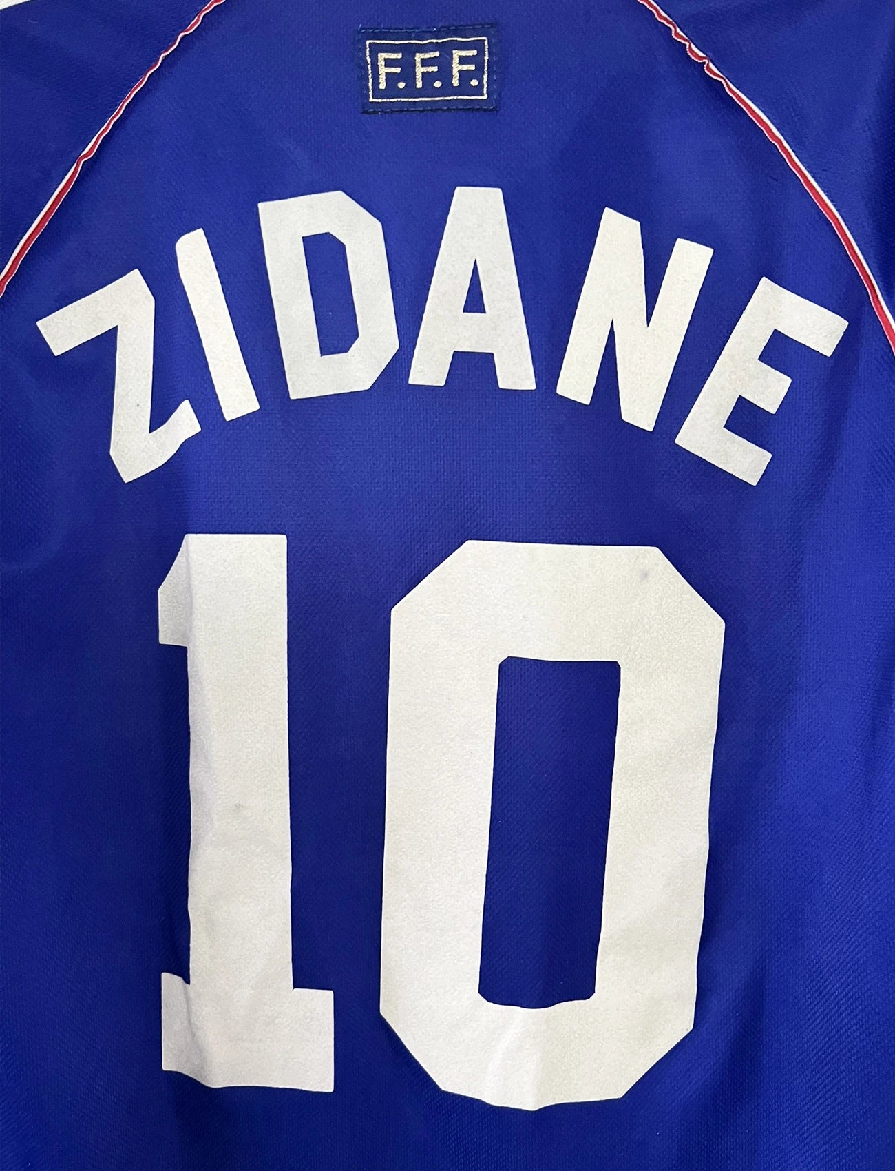 Maillot de foot vintage domicile bleu de l'Equipe de France 1998. On peut retrouver l'équipementier Adidas. Le maillot est floqué Zinedine Zidane. Il s'agit d'un maillot authentique d'époque.