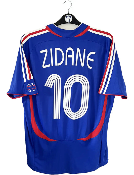 Maillot de foot vintage domicile bleu, blanc et rouge de l'équipe de france 2006. On peut retrouver l'équipementier adidas. Le maillot est floqué du numéro 10 Zinedine Zidane. Il s'agit d'un maillot authentique d'époque comportant l'étiquette 740126. Le maillot est un taille XL