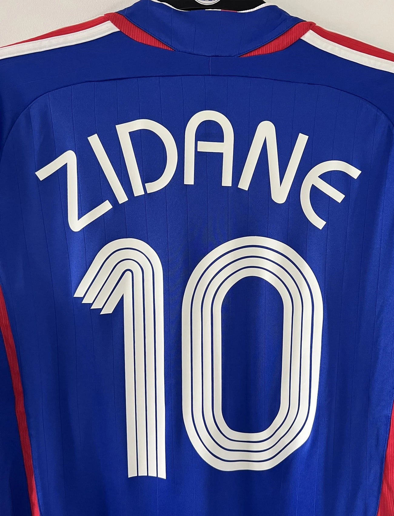 Maillot de foot vintage domicile bleu de l'équipe de france 2006. On peut retrouver l'équipementier adidas. Le maillot est floqué du numéro 10 Zinedine Zidane. Il s'agit d'un maillot authentique comportant l'étiquette 740126.