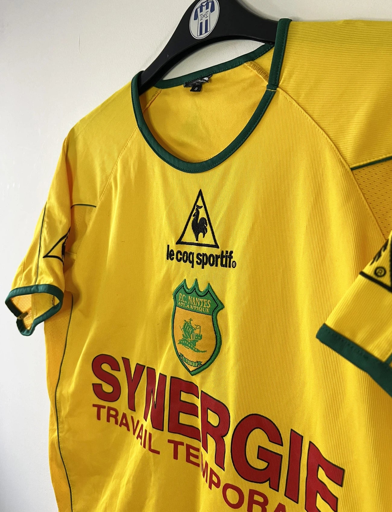 Maillot de foot vintage domicile jaune du FC Nantes de la saison 2003-2004. On peut retrouver l'équipementier Le Coq Sportif et le sponsor Synergie. Il s'agit d'un maillot authentique d'époque.