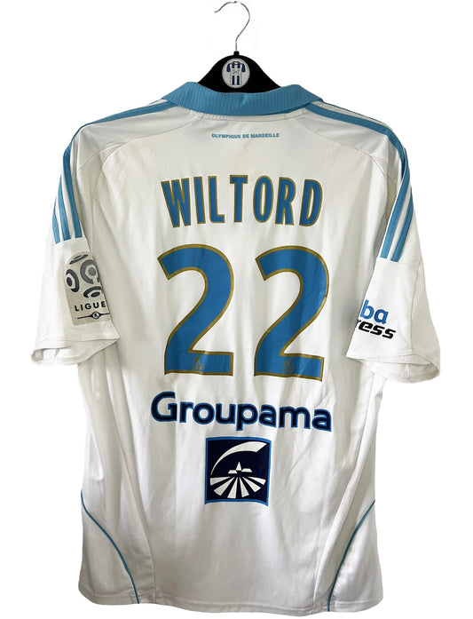 Maillot de foot vintage domicile blanc et bleu de l'om de la saison 2008-2009. On peut retrouver l'équipementier adidas, le sponsor direct energie, groupama et nasuba express. Le maillot est floqué du numéro 22 Wiltord. Il s'agit d'un maillot authentique d'époque comportant l'étiquette 314635