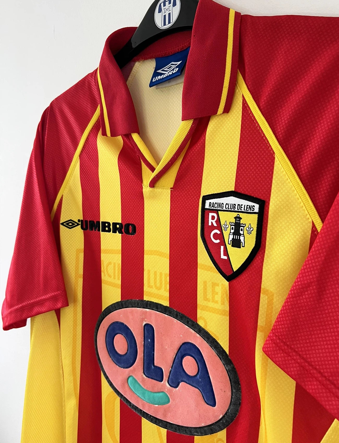 Maillot de foot vintage domicile rouge et jaune du RC Lens de la saison 1998/1999. On peut retrouver l'équipementier Umbro et le sponsor OLA. Il s'agit d'un maillot authentique d'époque.