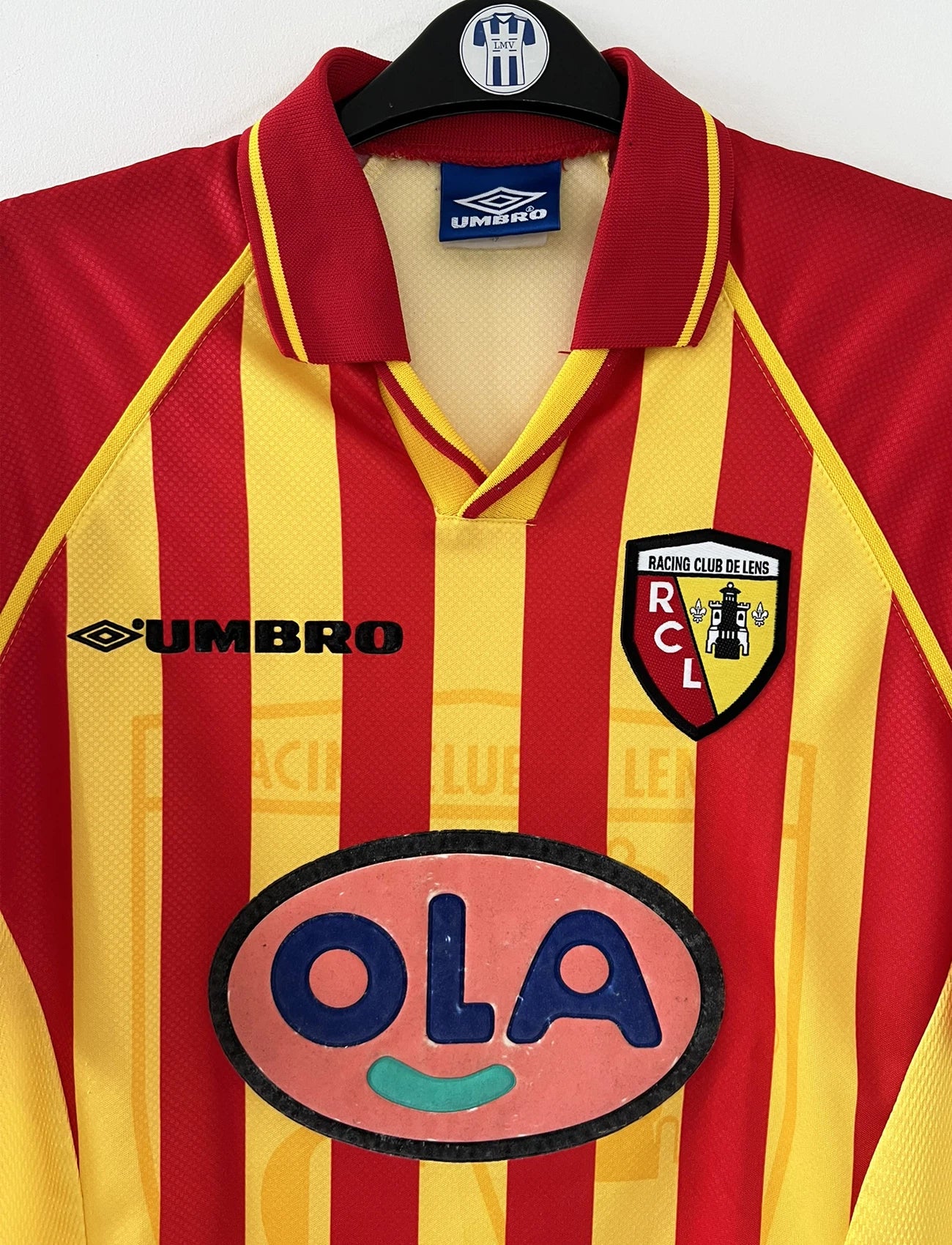 Maillot de foot vintage domicile rouge et jaune du RC Lens de la saison 1998/1999. On peut retrouver l'équipementier Umbro et le sponsor OLA. Il s'agit d'un maillot authentique d'époque.