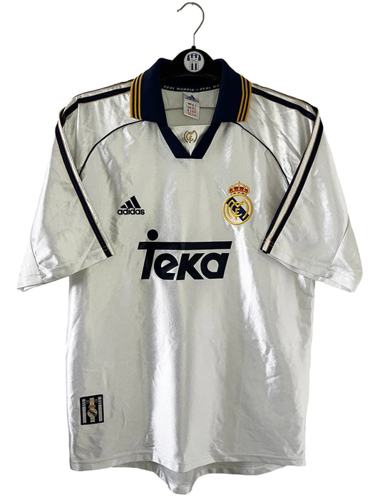 Maillot de foot vintage domicile blanc du Real Madrid de la saison 1998/1999. On peut retrouver l'équipementier Adidas et le sponsor Teka. Il s'agit d'un maillot authentique d'époque.