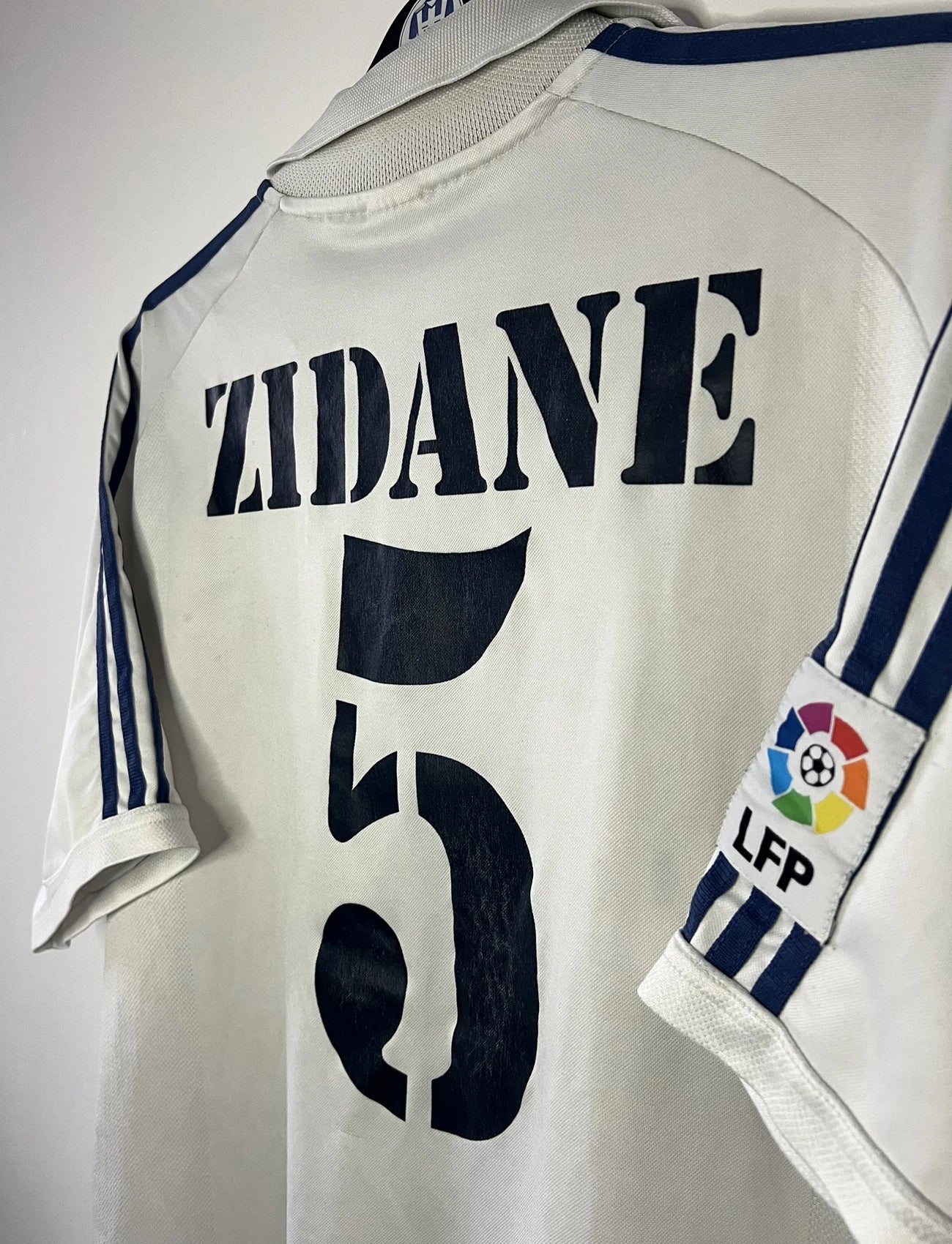 Maillot de foot vintage domicile du real madrid de la saison 2001-2002. Le maillot est de couleur blanc et noir. On peut retrouver l'équipementier adidas et le sponsor Real Madrid.com. Le maillot est floqué du numéro 5 Zinedine Zidane. Il s'agit d'un maillot authentique comportant les numéros 695856