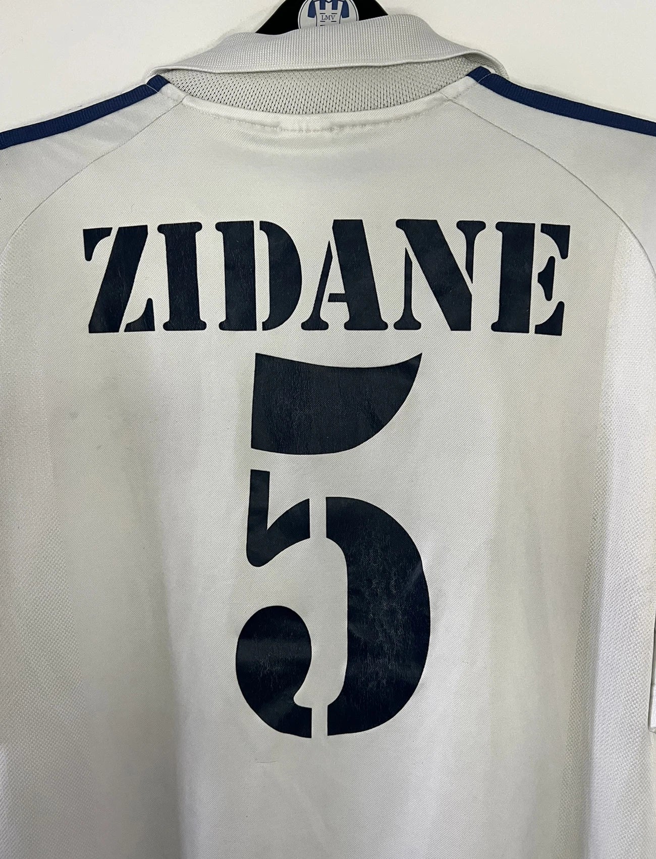 Maillot de foot vintage domicile du real madrid de la saison 2001-2002. Le maillot est de couleur blanc et noir. On peut retrouver l'équipementier adidas et le sponsor Real Madrid.com. Le maillot est floqué du numéro 5 Zinedine Zidane. Il s'agit d'un maillot authentique comportant les numéros 695856