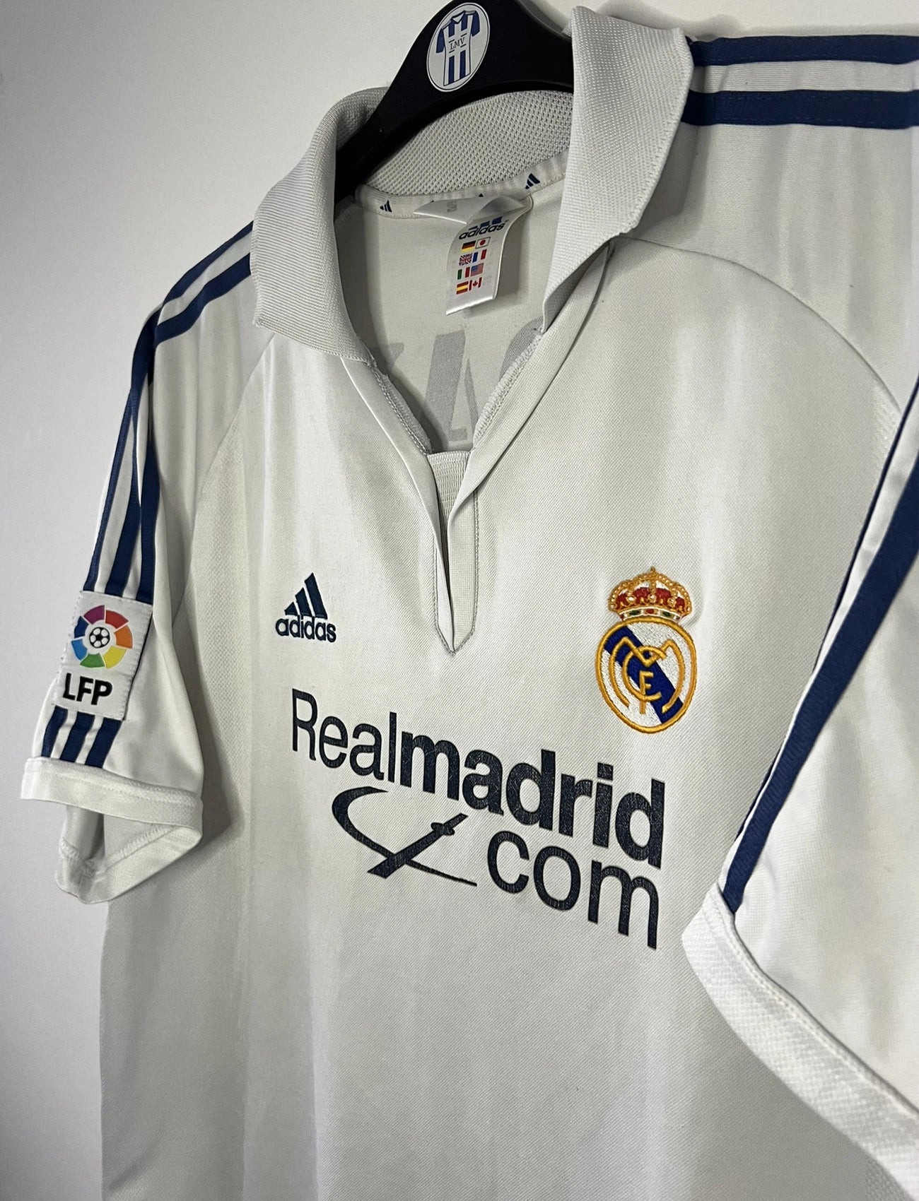 Maillot de foot vintage domicile du real madrid de la saison 2001-2002. Le maillot est de couleur blanc et noir. On peut retrouver l'équipementier adidas et le sponsor Real Madrid.com. Le maillot est floqué du numéro 5 Zinedine Zidane. Il s'agit d'un maillot authentique comportant les numéros 695856