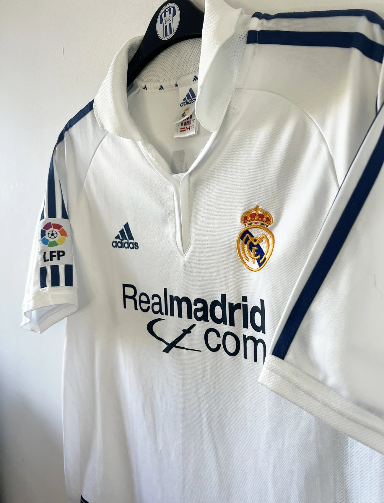 Maillot de foot vintage domicile du real madrid de la saison 2001-2002. Le maillot est de couleur blanc et noir. On peut retrouver l'équipementier adidas et le sponsor Real Madrid.com. Le maillot est floqué du numéro 5 Zinedine Zidane. Il s'agit d'un maillot authentique comportant les numéros 695856