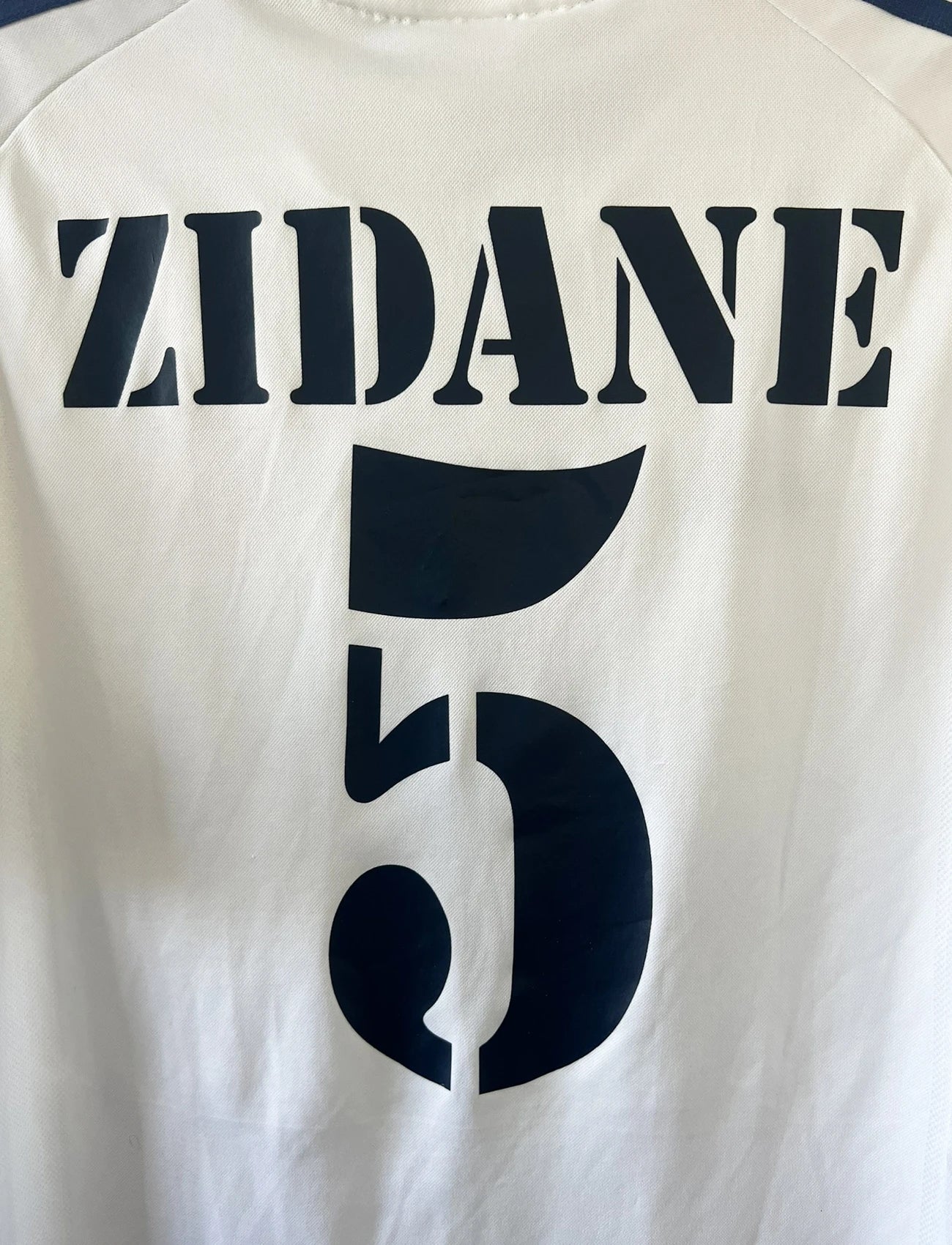 Maillot de foot vintage domicile du real madrid de la saison 2001-2002. Le maillot est de couleur blanc et noir. On peut retrouver l'équipementier adidas et le sponsor Real Madrid.com. Le maillot est floqué du numéro 5 Zinedine Zidane. Il s'agit d'un maillot authentique comportant les numéros 695856