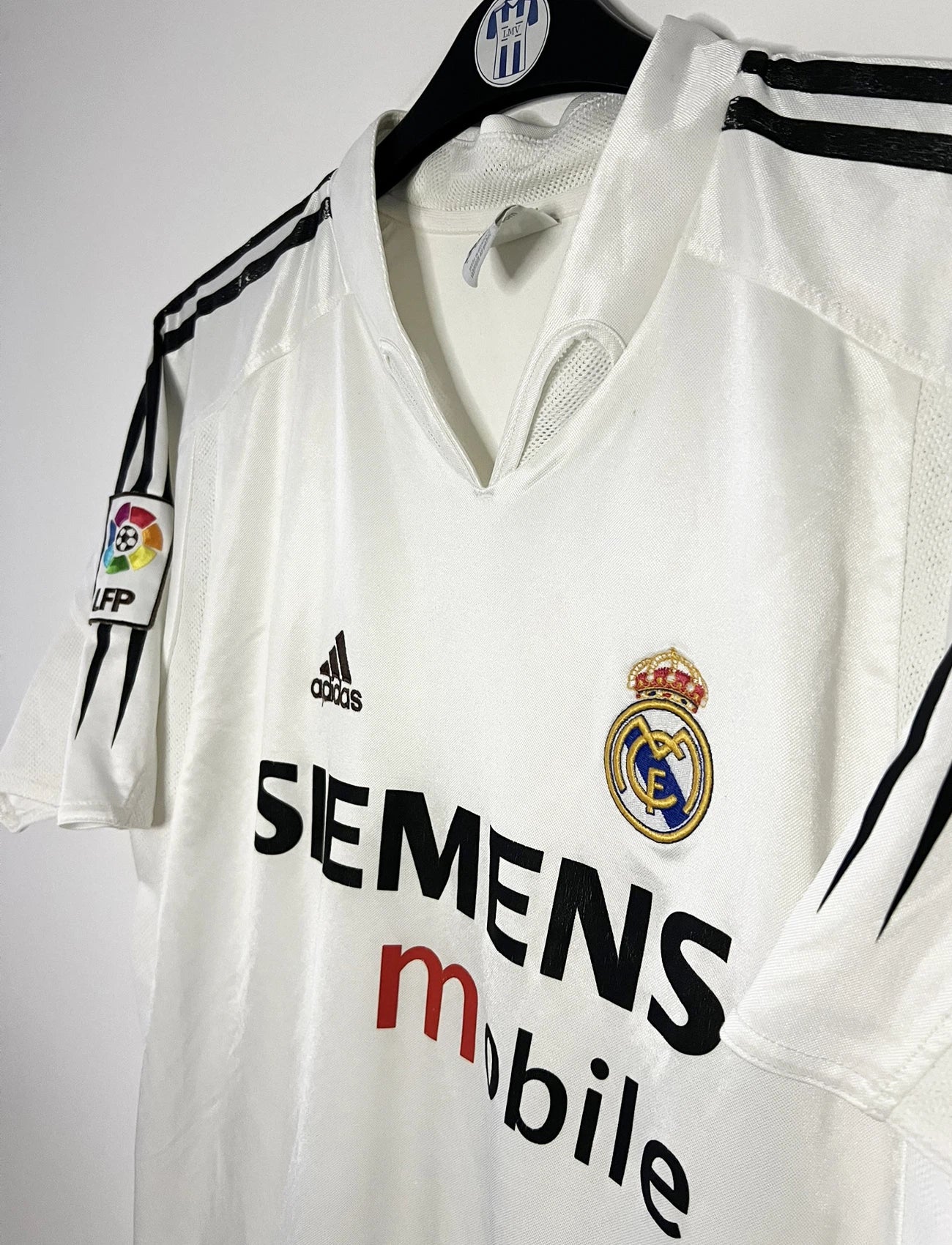 Maillot de foot vintage domicile blanc du real madrid de la saison 2004/2005. On peut retrouver l'équipementier Adidas et le sponsor Siemens. Il s'agit d'un maillot authentique d'époque comportant l'étiquette 367842