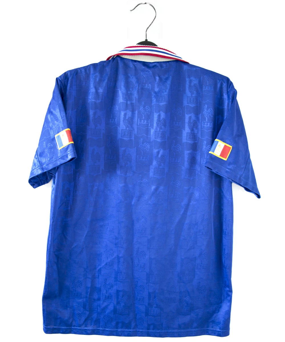 Maillot de foot vintage domicile de l'équipe de france 1996 de couleur bleu blanc et rouge. On peut retrouver l'équipementier adidas et le coq sans étoile. Il s'agit d'un maillot authentique d'époque.