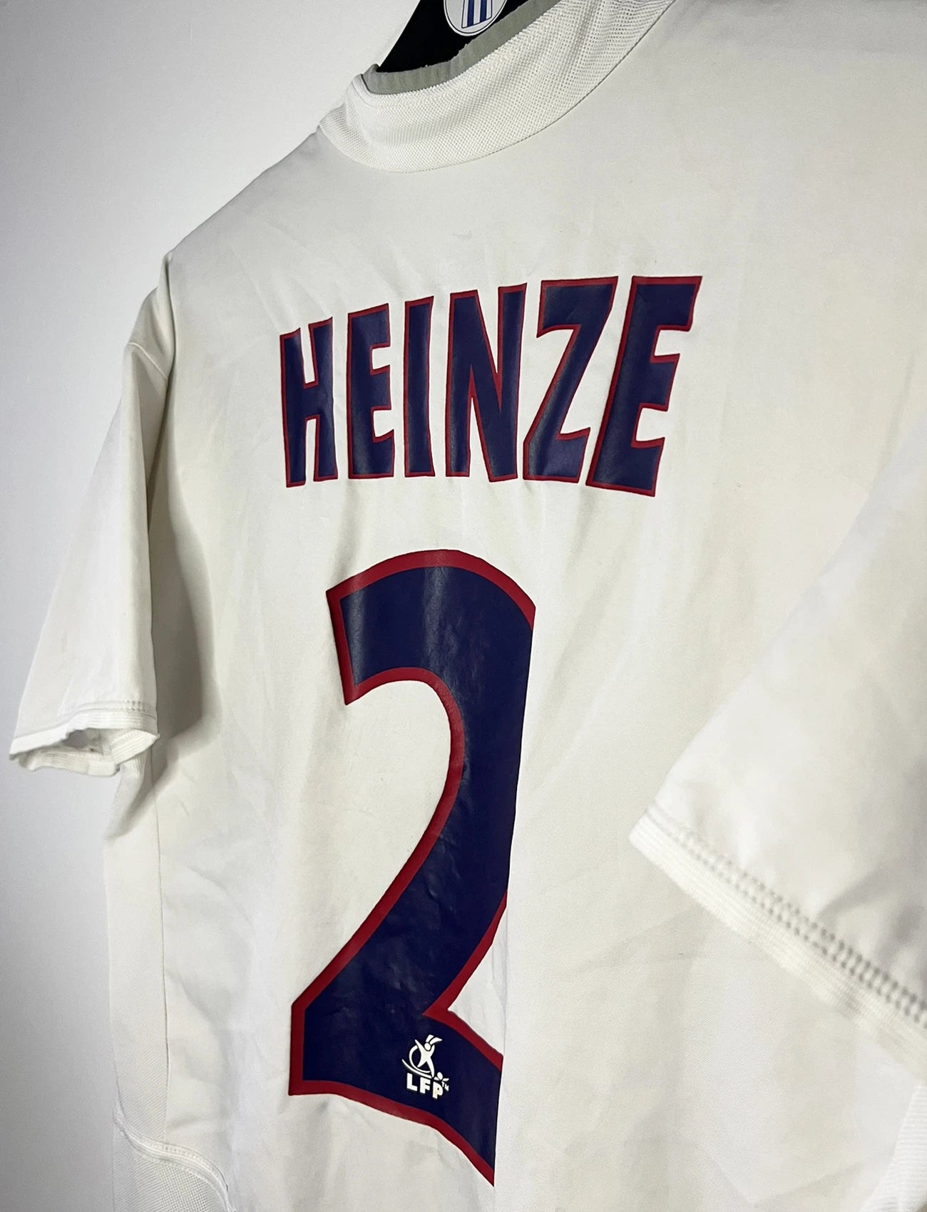 Maillot de foot vintage extérieur blanc du PSG de la saison 2002/2003. On peut retrouver l'équipementier Nike et le sponsor Thompson. Le maillot est floqué du numéro 2 Heinze. Il s'agit d'un maillot authentique d'époque comportant les numéros 184378.