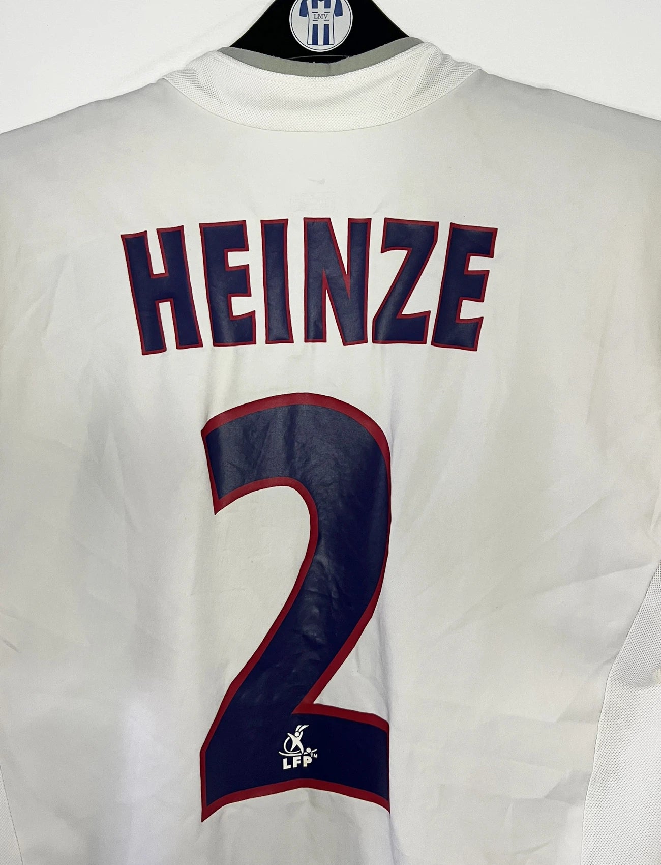 Maillot de foot vintage extérieur blanc du PSG de la saison 2002/2003. On peut retrouver l'équipementier Nike et le sponsor Thompson. Le maillot est floqué du numéro 2 Heinze. Il s'agit d'un maillot authentique d'époque comportant les numéros 184378.