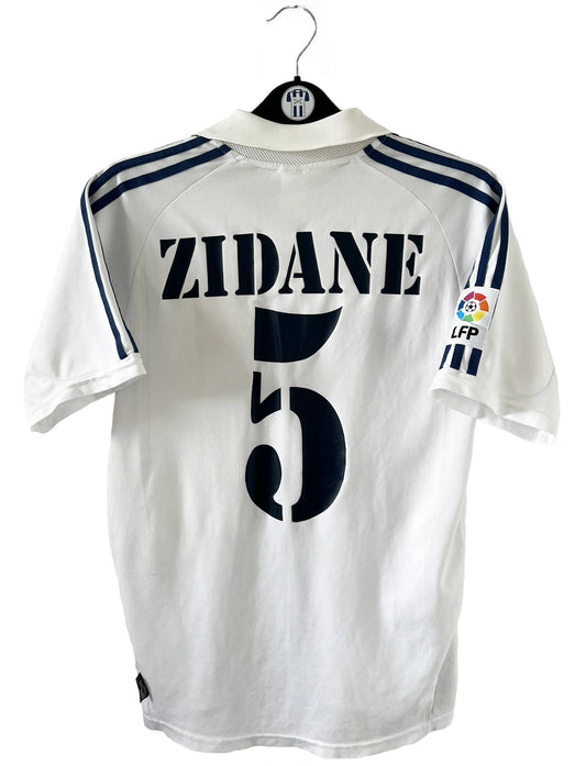 Maillot de foot vintage domicile du real madrid de la saison 2001-2002. Le maillot est de couleur blanc et noir. On peut retrouver l'équipementier adidas et le sponsor Real Madrid.com. Le maillot est floqué du numéro 5 Zinedine Zidane. Il s'agit d'un maillot authentique comportant les numéros 695856